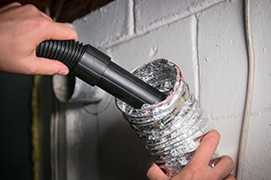 somone using a vacuum to clean a dryer duct vent